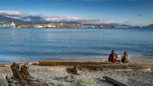 Tourists sitting near the lake in the Seawall of Stanley Park in Vancouver with the Lions Gate Bridge in the background towards North Vancouver.